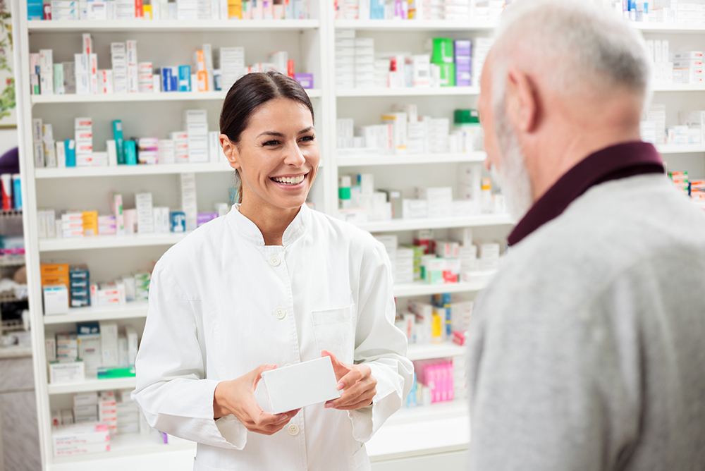 Caucasian Female Pharmacist talking to an older caucasian male about his prescription at the counter.